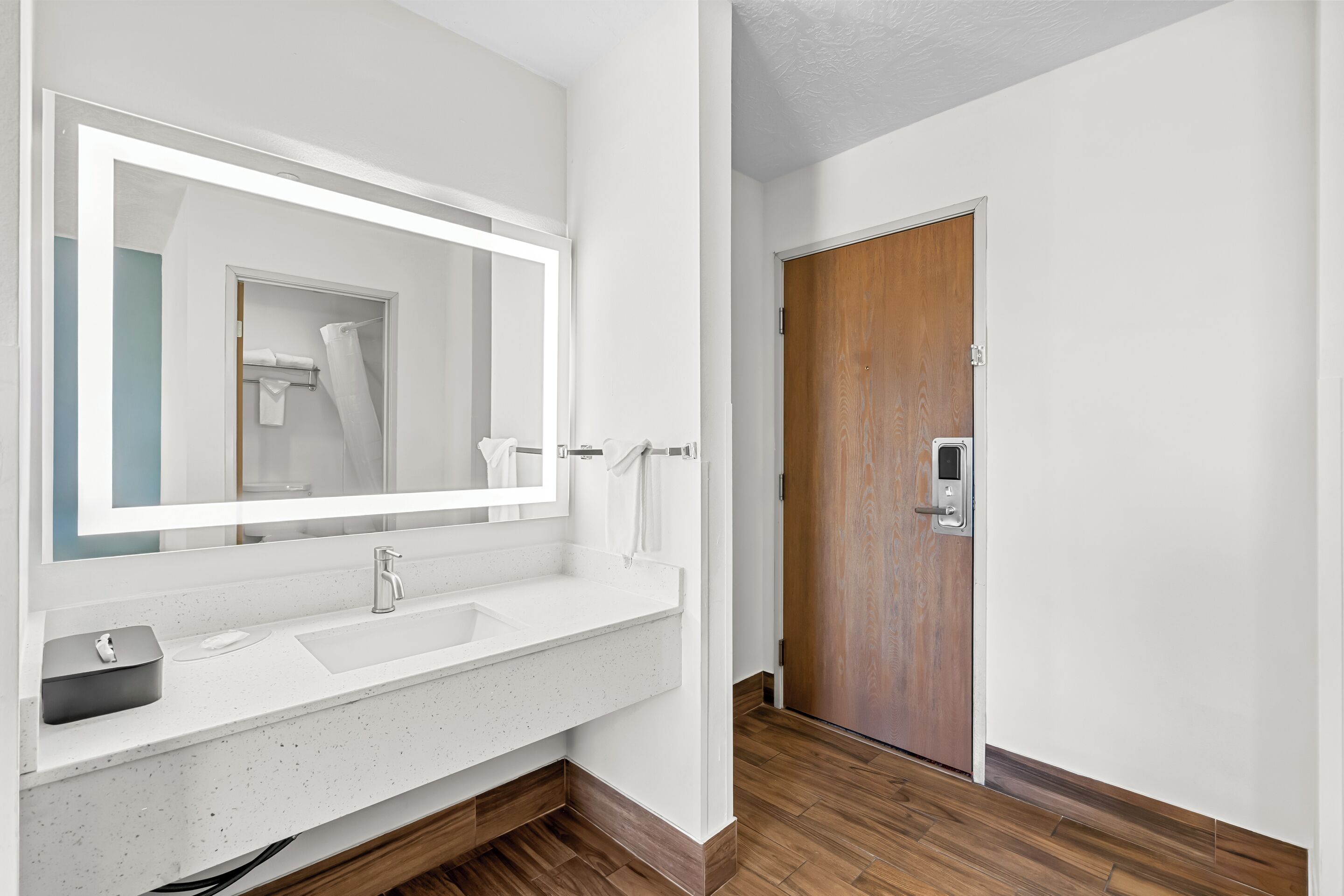 A modern bathroom with a white sink, a large mirror, and a wooden door.