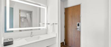 A modern bathroom with a white sink, a large mirror, and a wooden door.