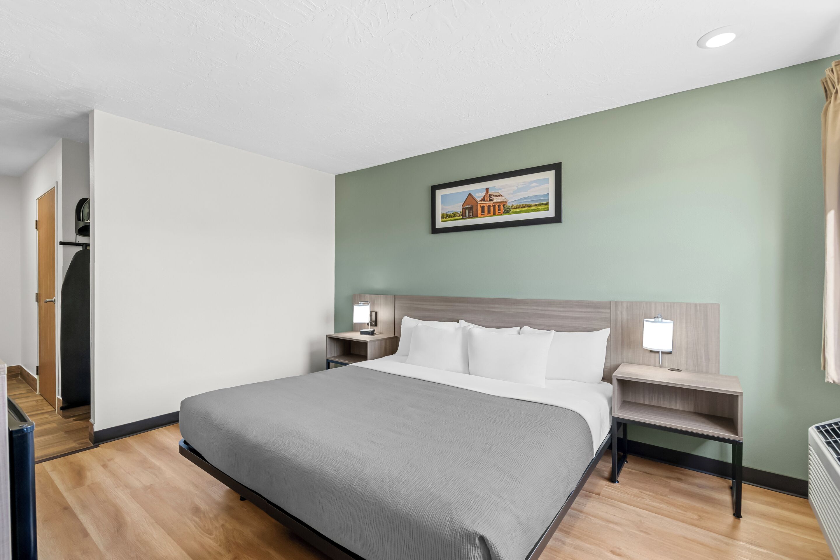 A hotel room with a large bed, two bedside tables with lamps, a framed picture on the wall, and a wooden floor.