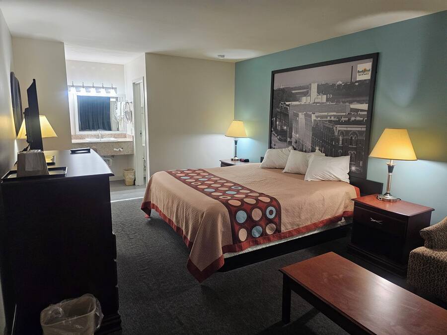 Une chambre d’hôtel avec un lit, deux lampes de chevet, un bureau, une chaise et un grand tableau représentant un paysage urbain accroché au mur.