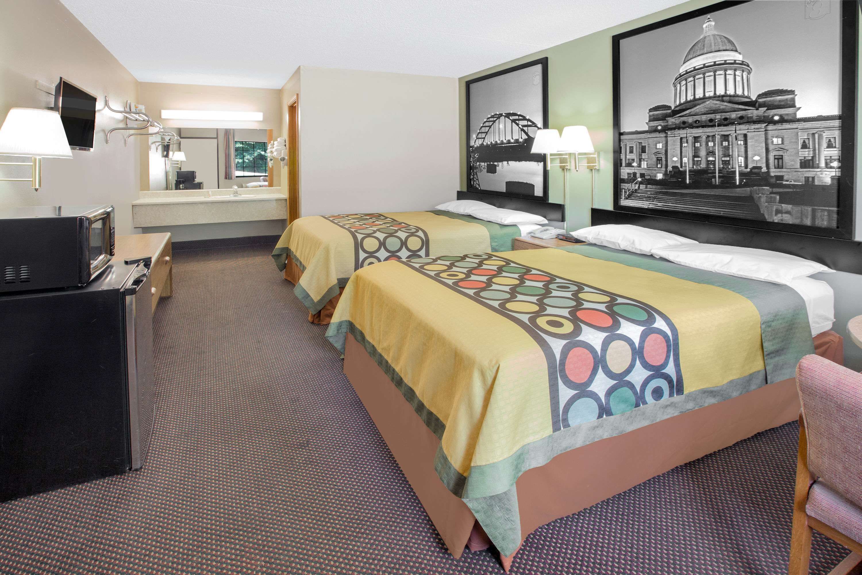 A hotel room with two beds, a desk with a TV, and a large framed picture of a building.