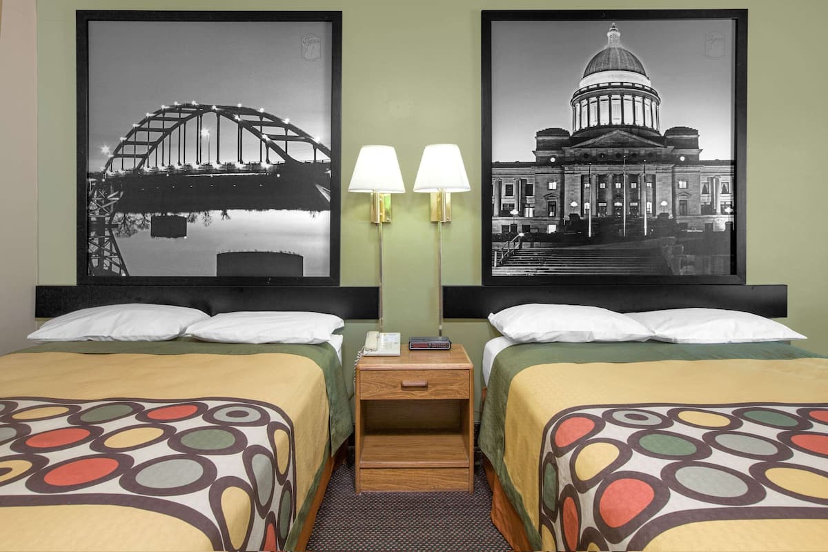 Une chambre d’hôtel avec deux lits, une table de chevet avec une lampe, et deux grandes photos encadrées représentant des ponts et un bâtiment.