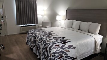 Habitación de hotel con una cama grande, dos lámparas de noche, un ventanal con cortinas, un equipo de aire acondicionado y una puerta con cerradura.