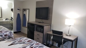 Una habitación de hotel con una cama, un escritorio con computadora, un televisor, un microondas y una lámpara.