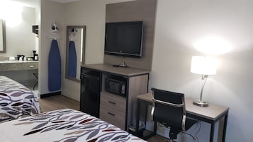 Una habitación de hotel con una cama, un escritorio con computadora, un televisor, un microondas y una lámpara.