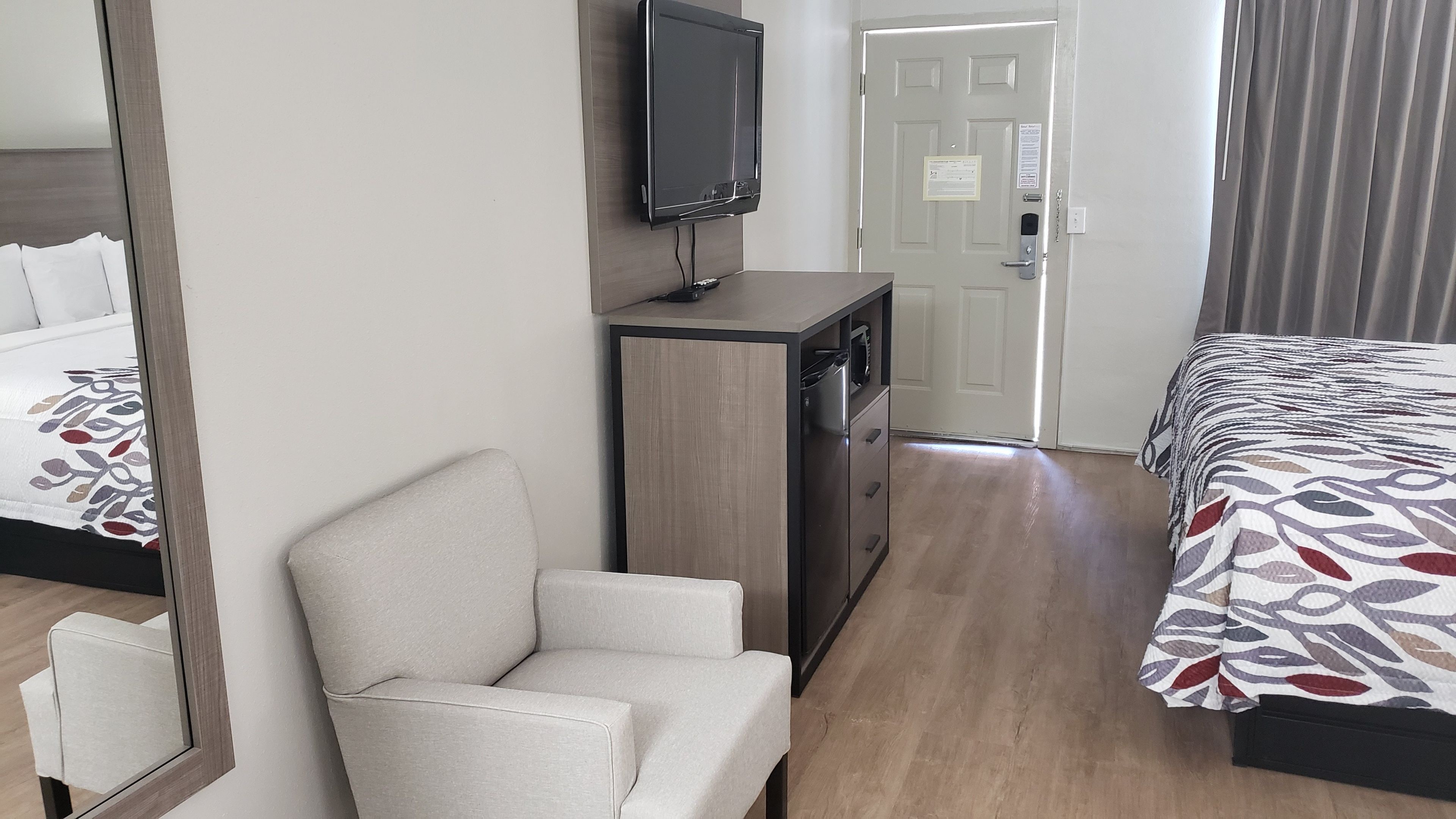 Una habitación de hotel con una cama, una silla, un escritorio y una puerta.