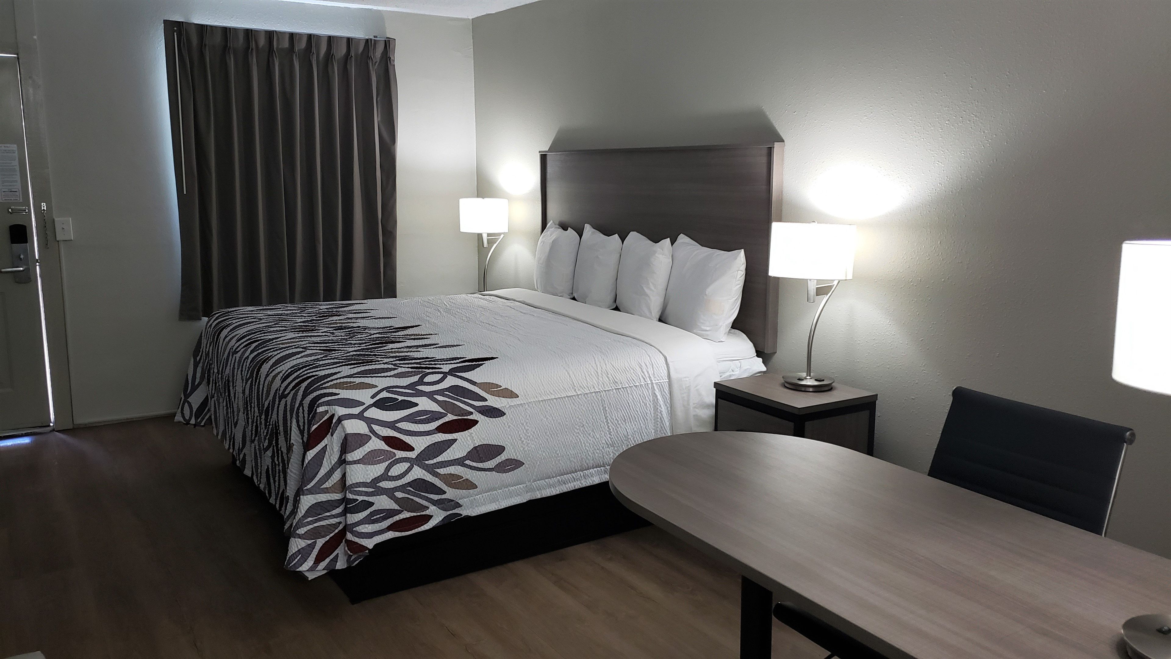 Una habitación de hotel con una cama, lámparas de noche, un escritorio y una silla.