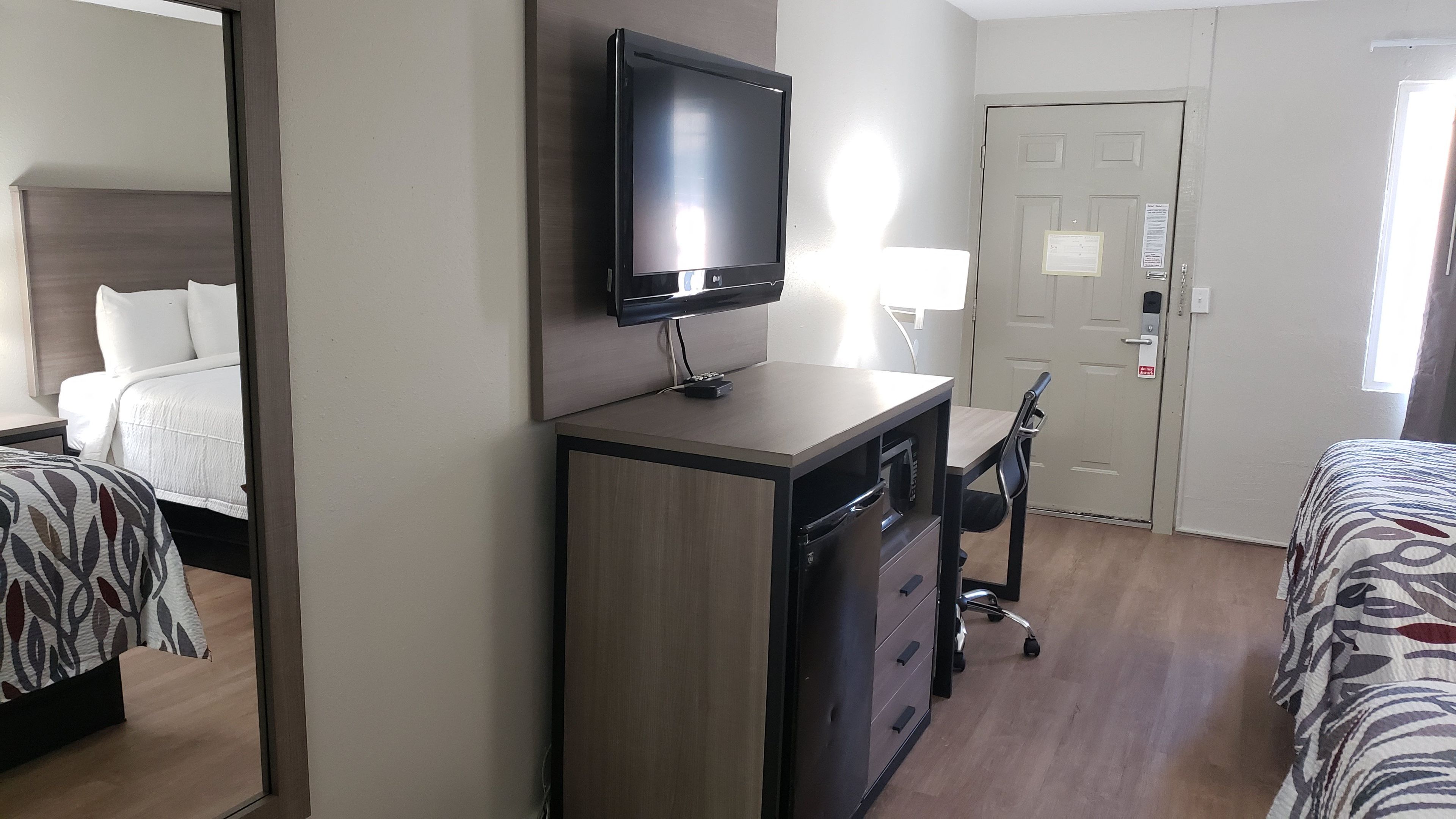 A hotel room with a bed, a desk with a television, a chair, and a door.