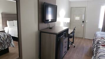 A hotel room with a bed, a desk with a television, a chair, and a door.
