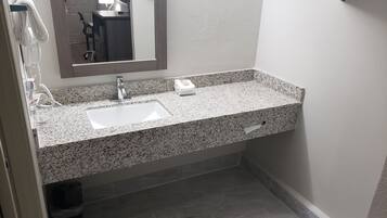 A bathroom with a granite countertop, a white sink, a mirror, and a towel rack.