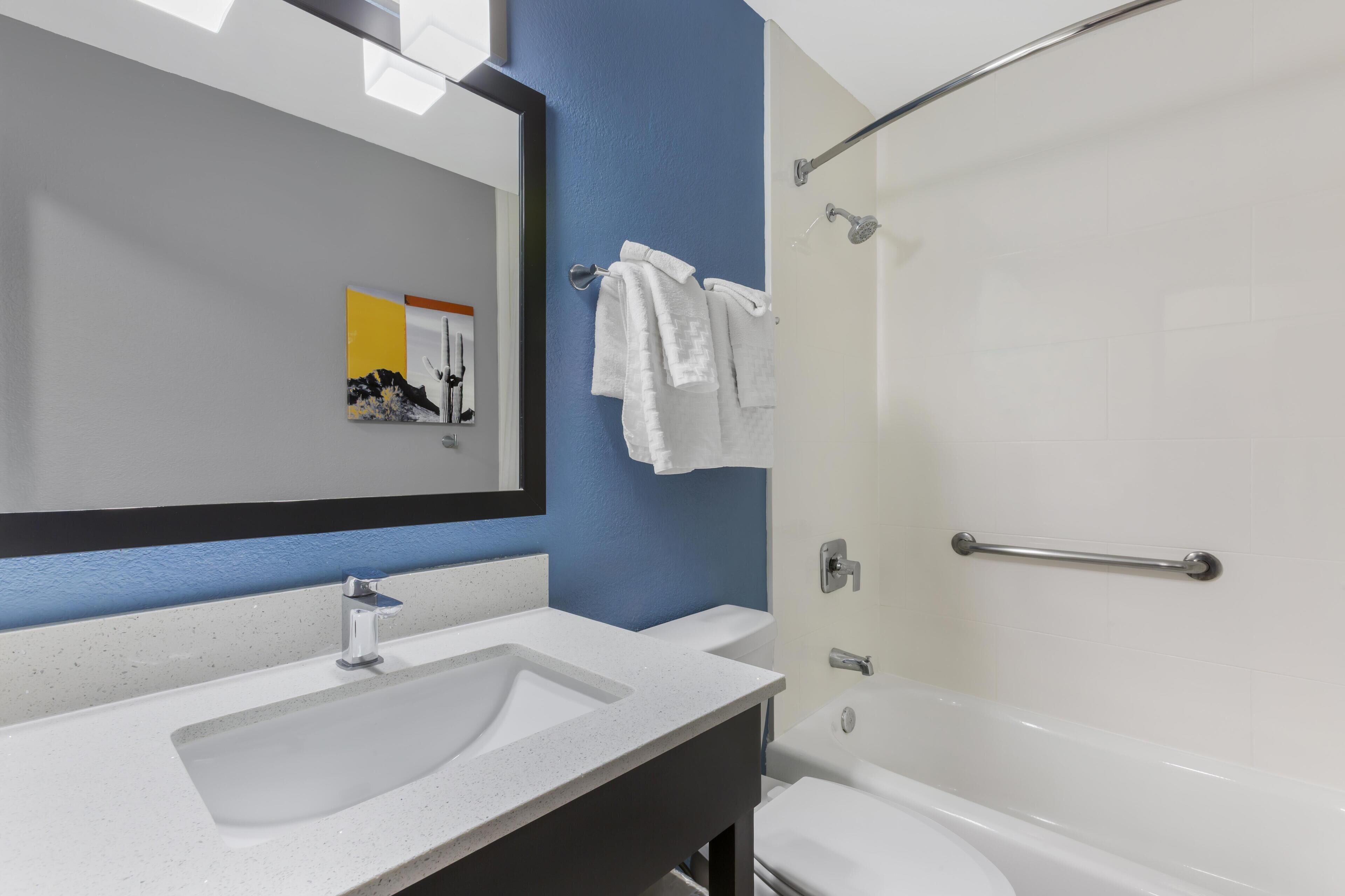 Un baño con un lavamanos blanco, un espejo grande y una bañera blanca.