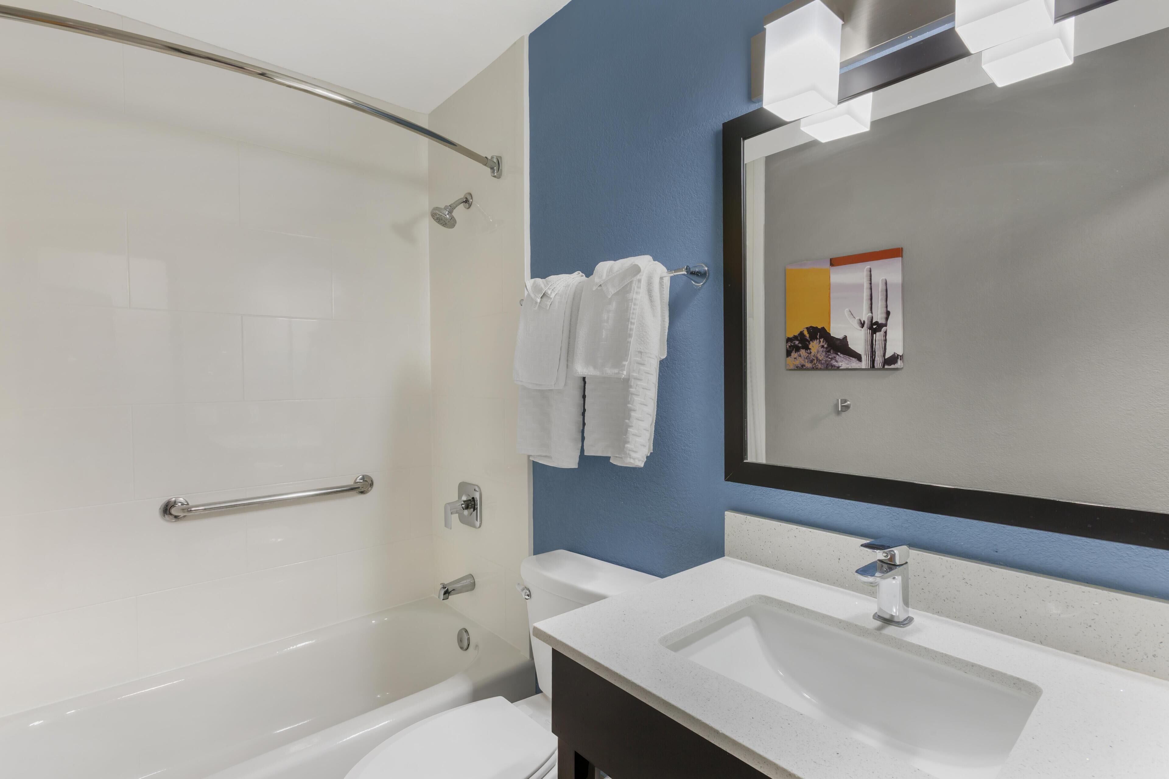 A modern bathroom with a shower, toilet, and sink, featuring a blue accent wall and a large mirror.