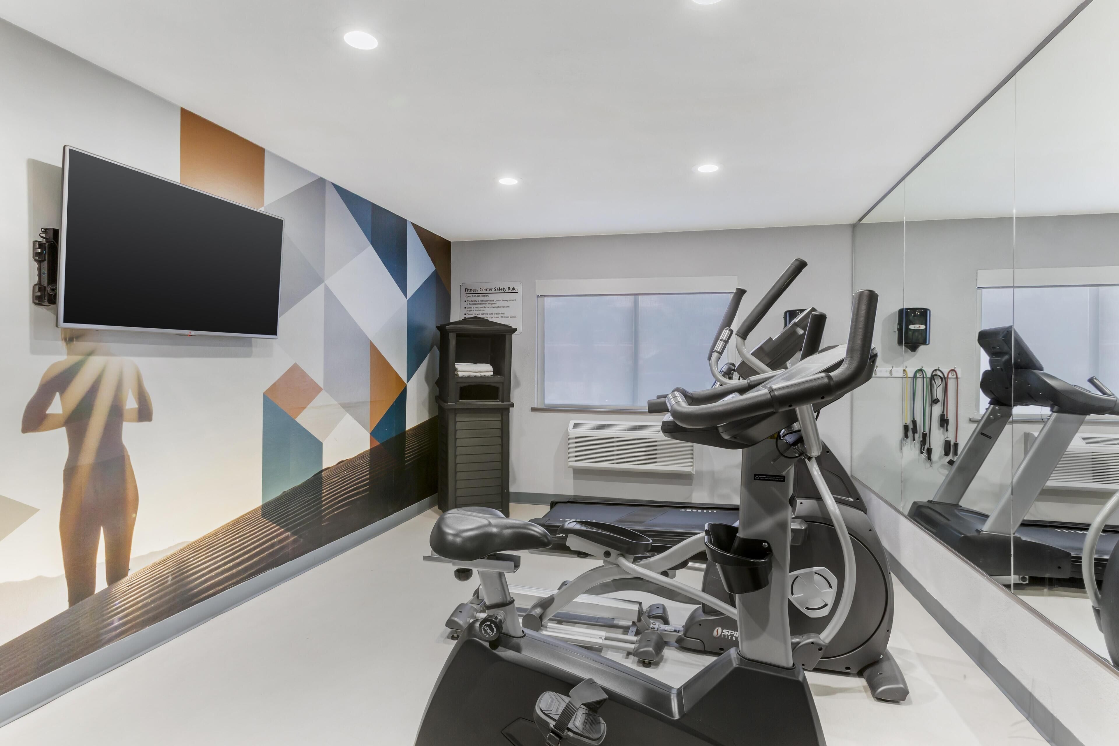 A modern gym with exercise equipment, a large mirror, and a TV on the wall.