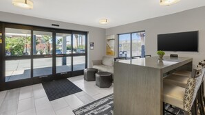 A modern hotel lobby with a reception desk, seating area, and large windows offering a view of the street.