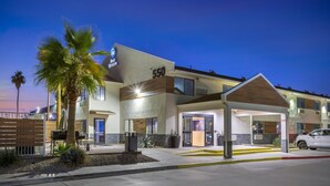 A modern hotel with a covered entrance, outdoor seating, and palm trees.