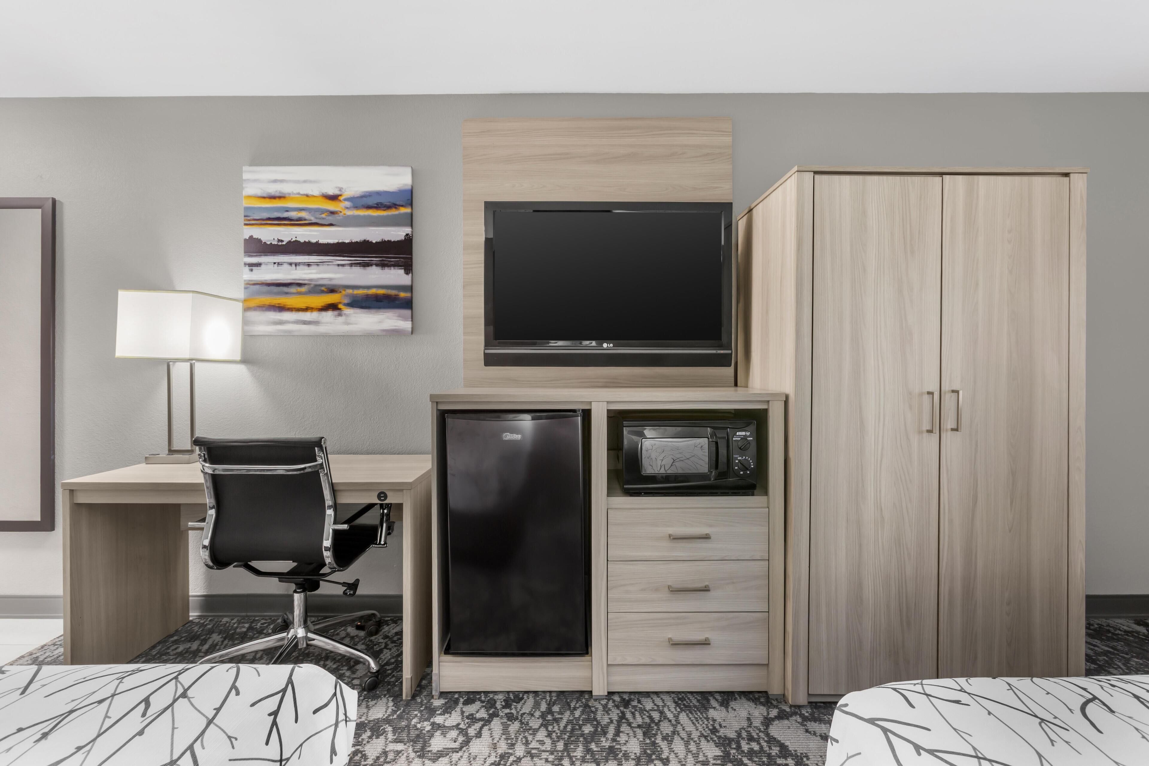 Een hotelkamer met een bureau, stoel, televisie, minibar, kledingkast en twee bedden.