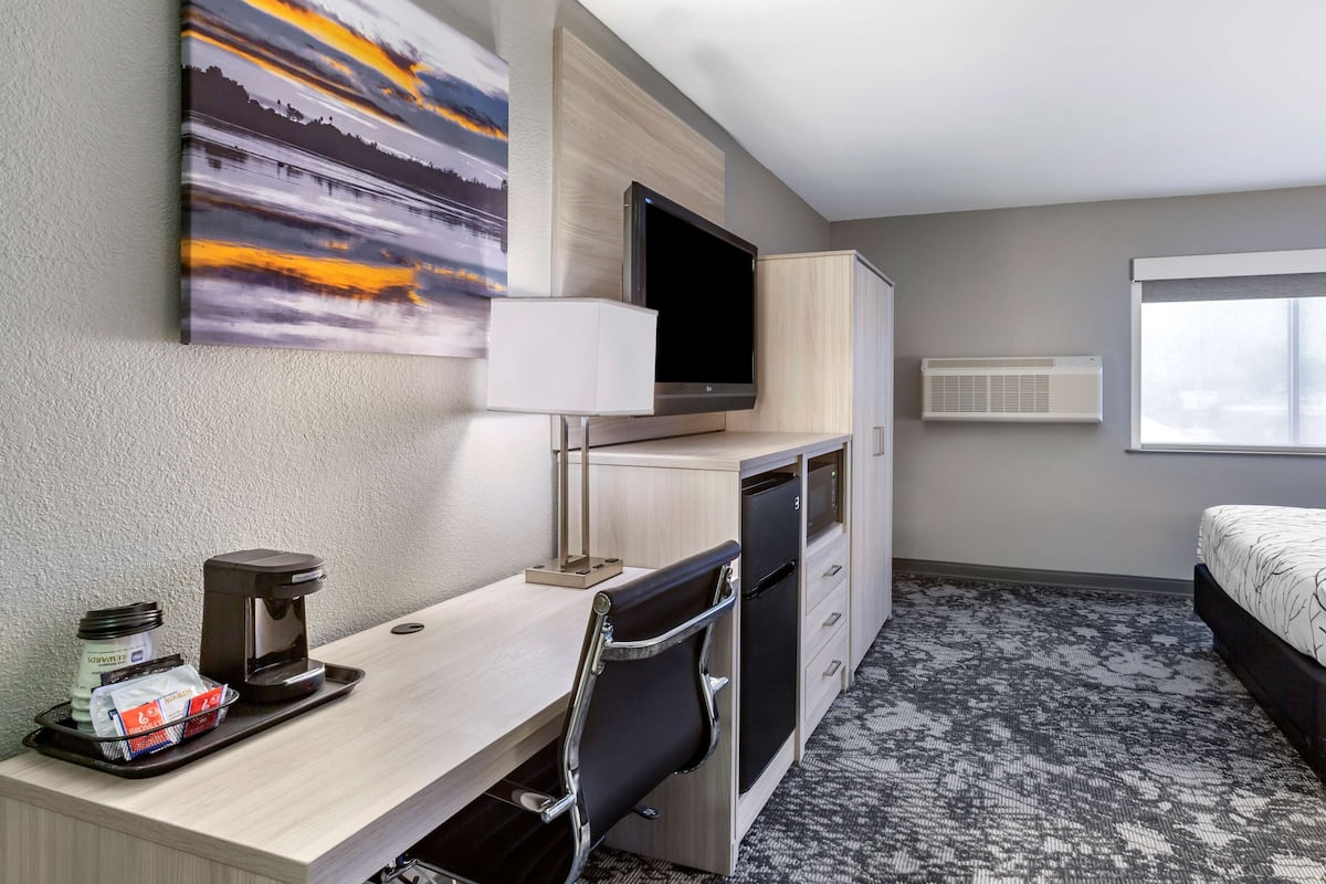 A hotel room with a bed, a desk with a coffee maker, a TV, and a painting on the wall.