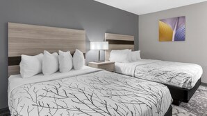 A hotel room with two beds, a nightstand, a lamp, and a painting on the wall.
