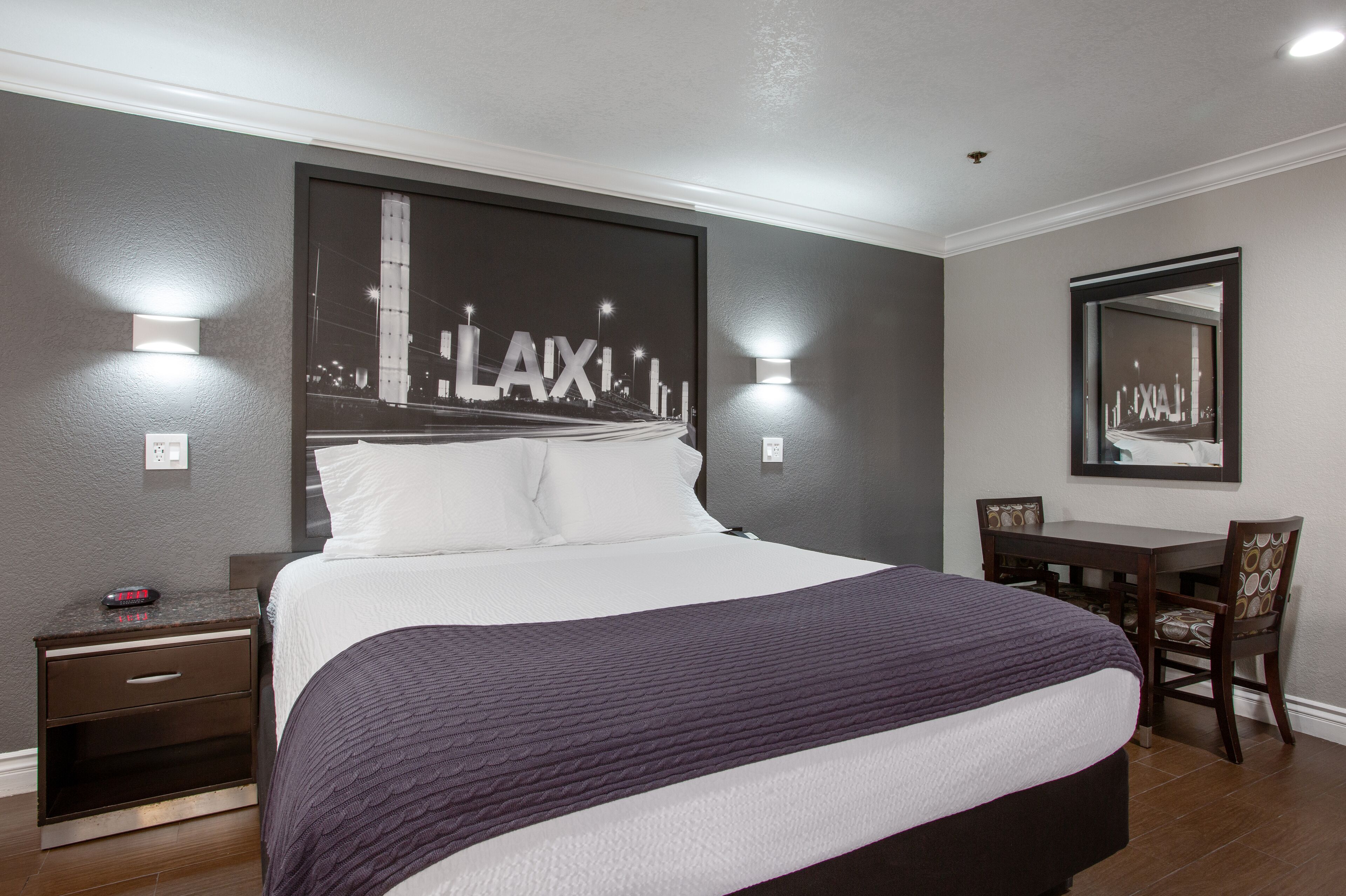 Een hotelkamer met een groot bed, een bureau en een stoel. Er hangt een ingelijst schilderij aan de muur en er is een spiegel boven het bureau.