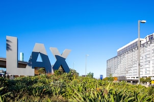 Un edificio con un gran letrero 'LAX' en primer plano, rodeado de follaje.