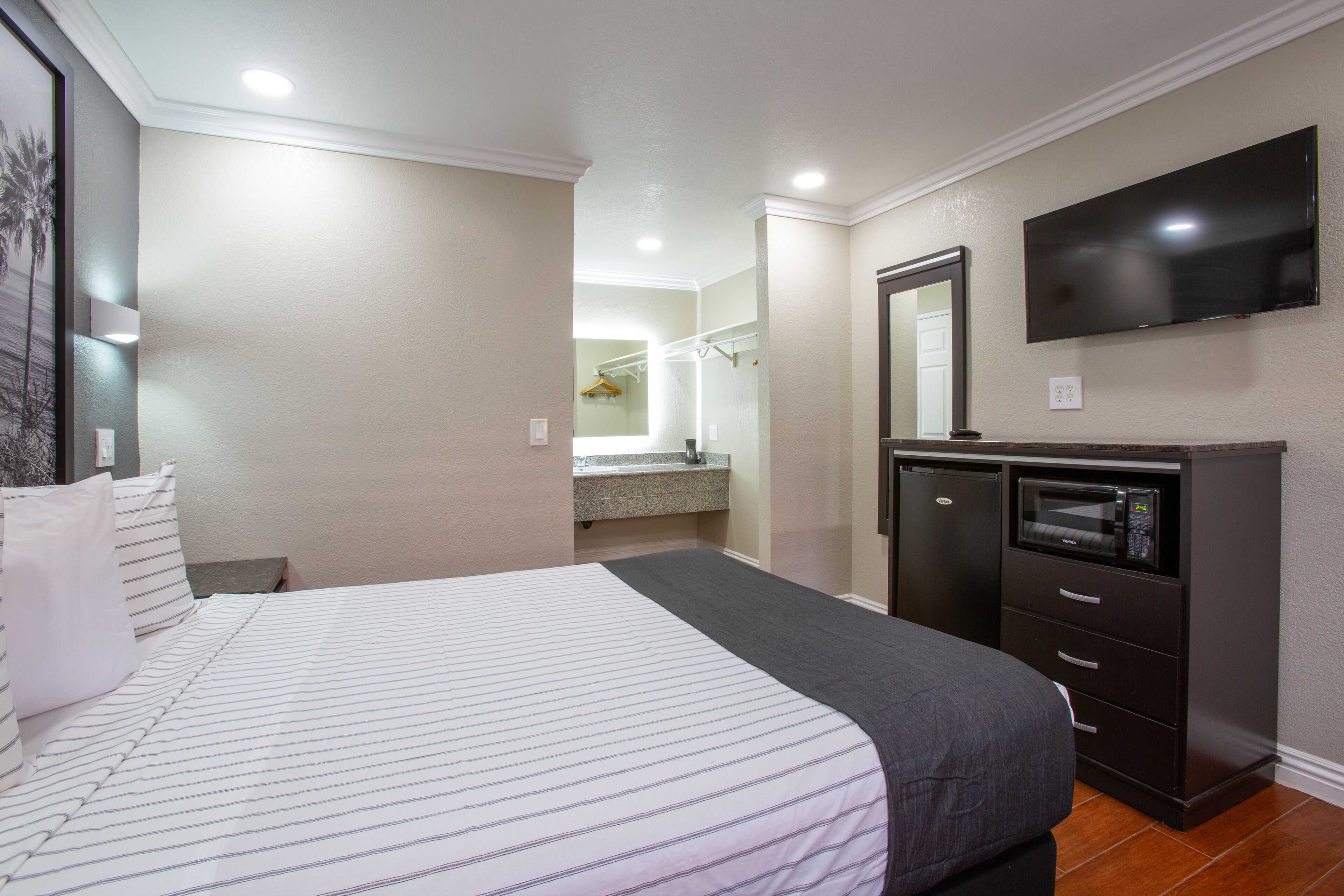 A hotel room with a bed, a dresser, a television, and a bathroom visible in the background.