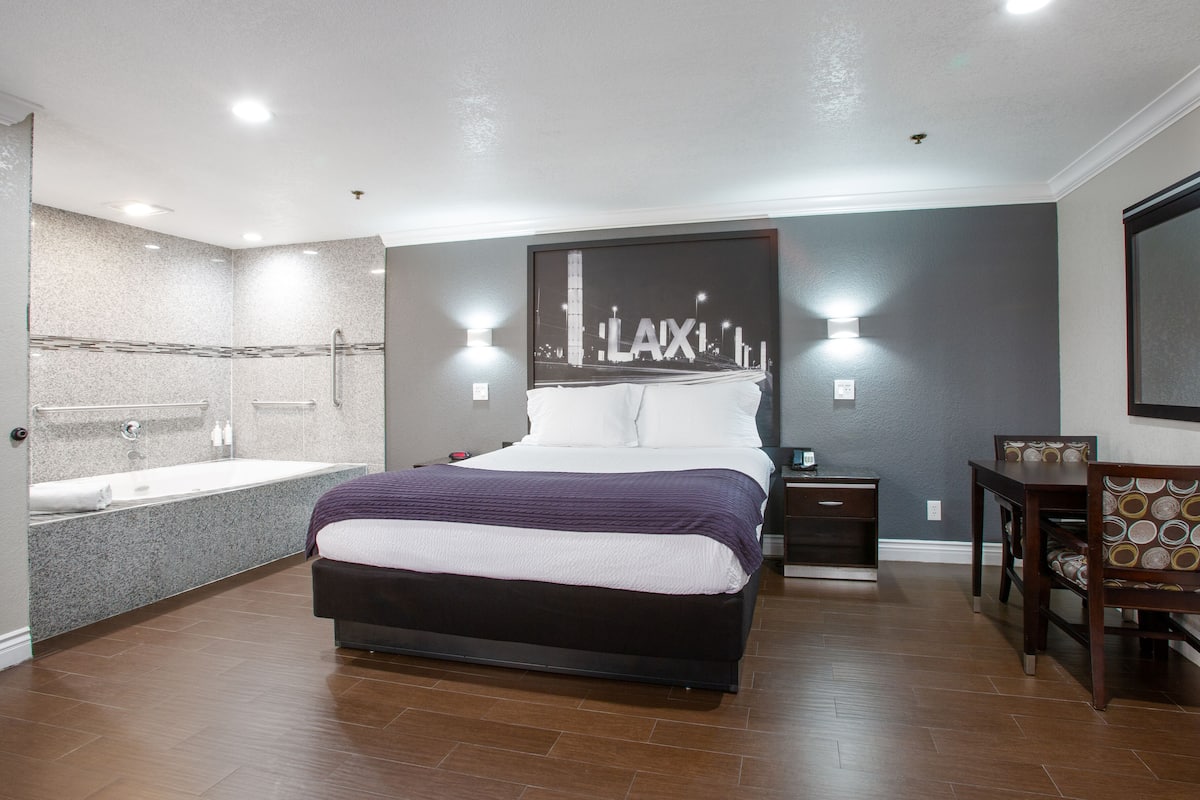 A modern hotel room with a large bed, a separate bathroom with a bathtub, a desk, and a chair.