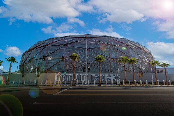 A modern, dome-shaped building with a transparent facade, palm trees in front, and a clear sky.