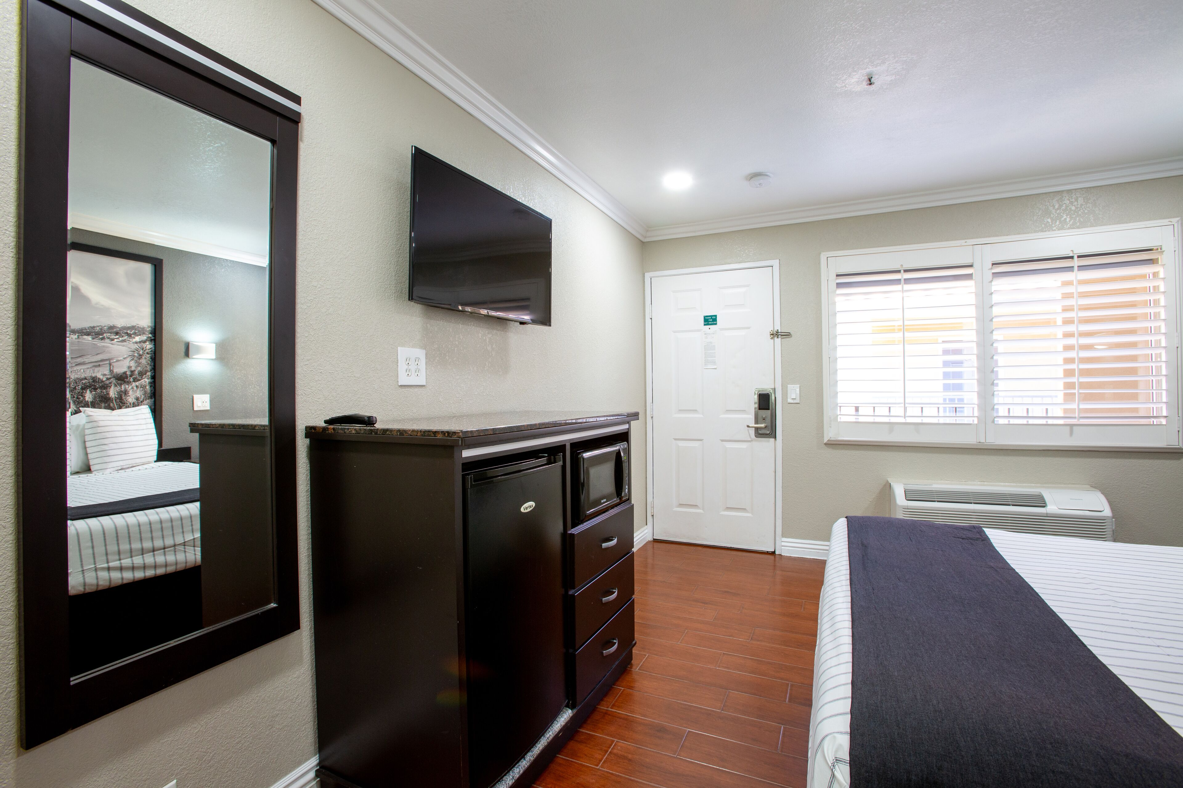A hotel room with a bed, a dresser, a television, a door, and a window with blinds.