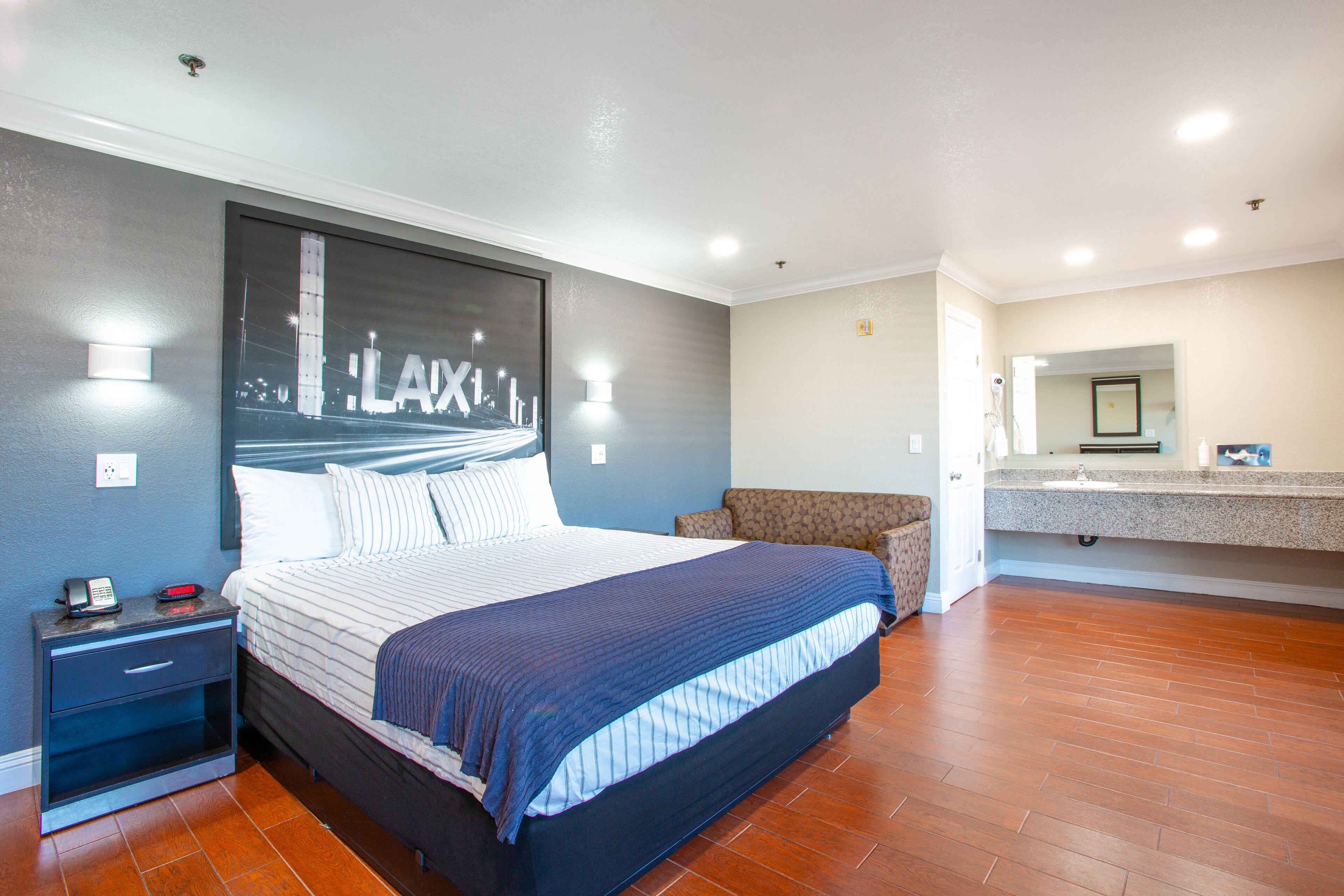 Un dormitorio moderno con una cama grande, una mesita de noche, un área de descanso y un baño con espejo y lavabo.