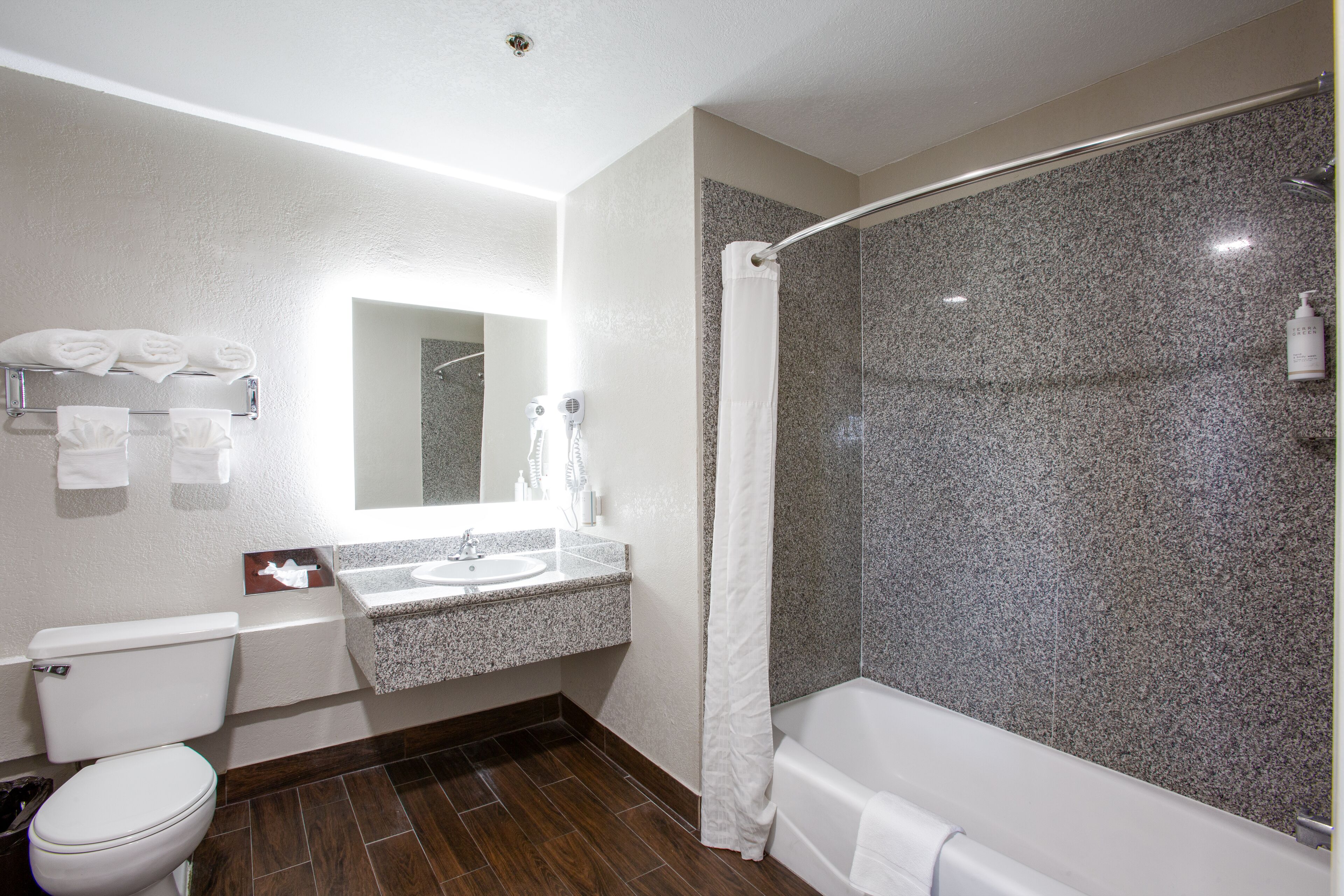 A modern bathroom with a granite countertop sink, a white toilet, a shower with a glass door, and a towel rack with folded towels.