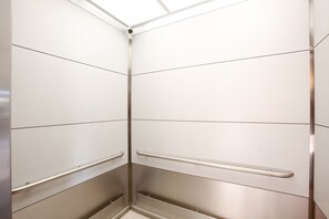 Rincón de una habitación con paredes blancas, una manija metálica y una sección inferior texturizada.