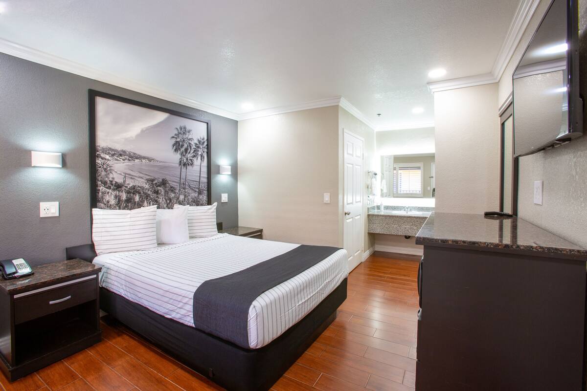 A hotel room with a large bed, a nightstand, a desk, and a kitchenette.