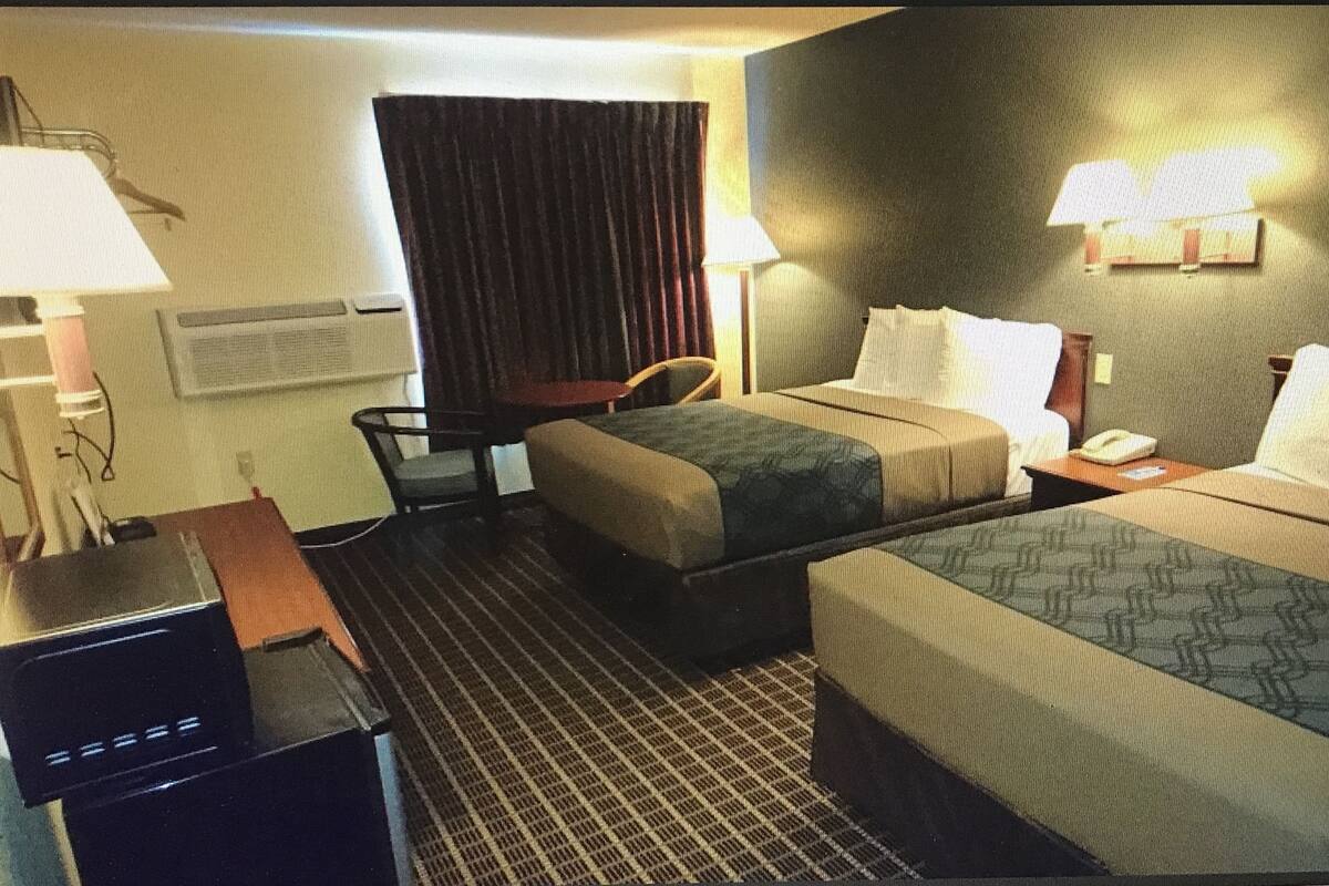 Ett hotellrum med två sängar, ett skrivbord, en stol, en lampa och ett fönster med gardiner.