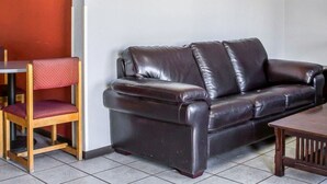Un canapé en cuir marron foncé avec une structure en bois, une chaise en bois avec un coussin rouge et une petite table en bois.