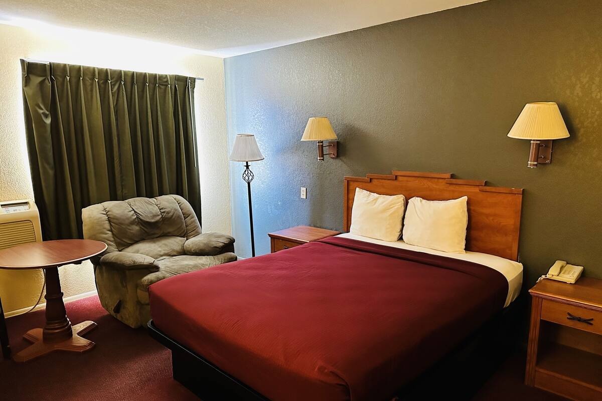 Ett hotellrum med en säng, en stol, en lampa och en telefon.