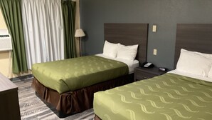 Une chambre d’hôtel avec deux lits, une table de chevet, une lampe et une fenêtre avec des rideaux.