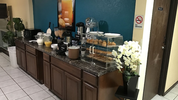 Un espace d’accueil d’hôtel avec un comptoir où sont exposés des articles pour le petit-déjeuner, une machine à café et un panneau indiquant les heures d’ouverture.