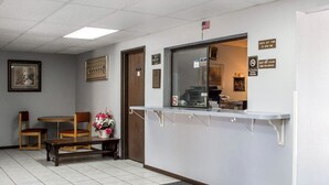 Un espace d’accueil comprenant un comptoir d’enregistrement, un banc en bois, une petite table ornée d’un vase de fleurs et des tableaux encadrés accrochés au mur.