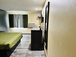 Una habitación de hotel con una cama, un escritorio, un espejo y un equipo de aire acondicionado.