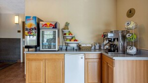 A kitchenette with a refrigerator, a juice dispenser, a coffee maker, and a fruit display. - Rodeway Inn Asheville (Asheville)