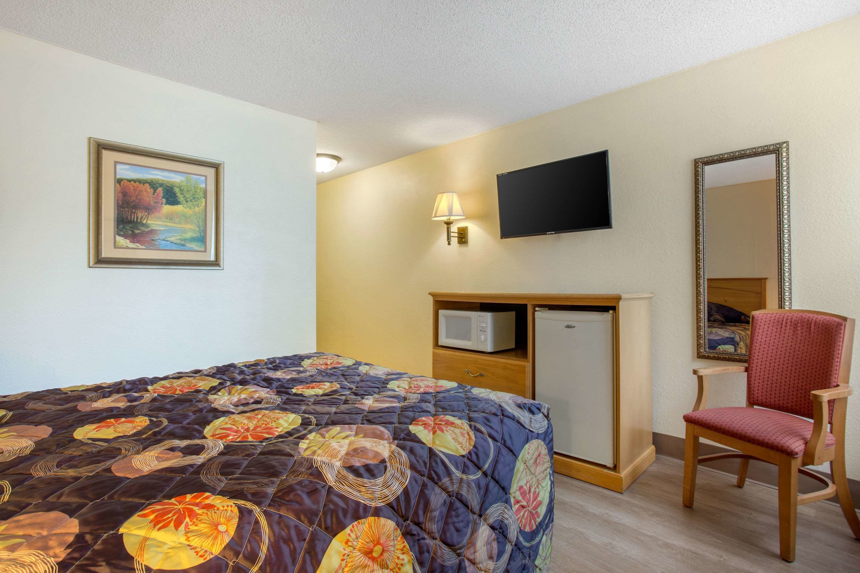 Habitación de hotel con una cama, televisión, microondas, una silla y un cuadro en la pared.