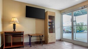 A room with a desk, a lamp, a television mounted on the wall, a glass cabinet with shelves, and a large window offering a view of the outside. - Rodeway Inn Asheville (Asheville)