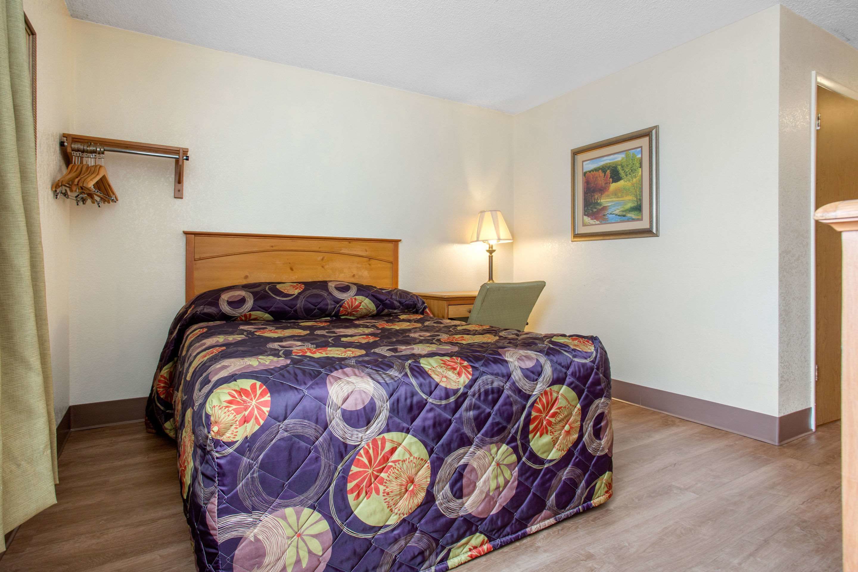 Une chambre d’hôtel avec un lit, une table de chevet, une lampe, un tableau au mur et un porte-manteau.