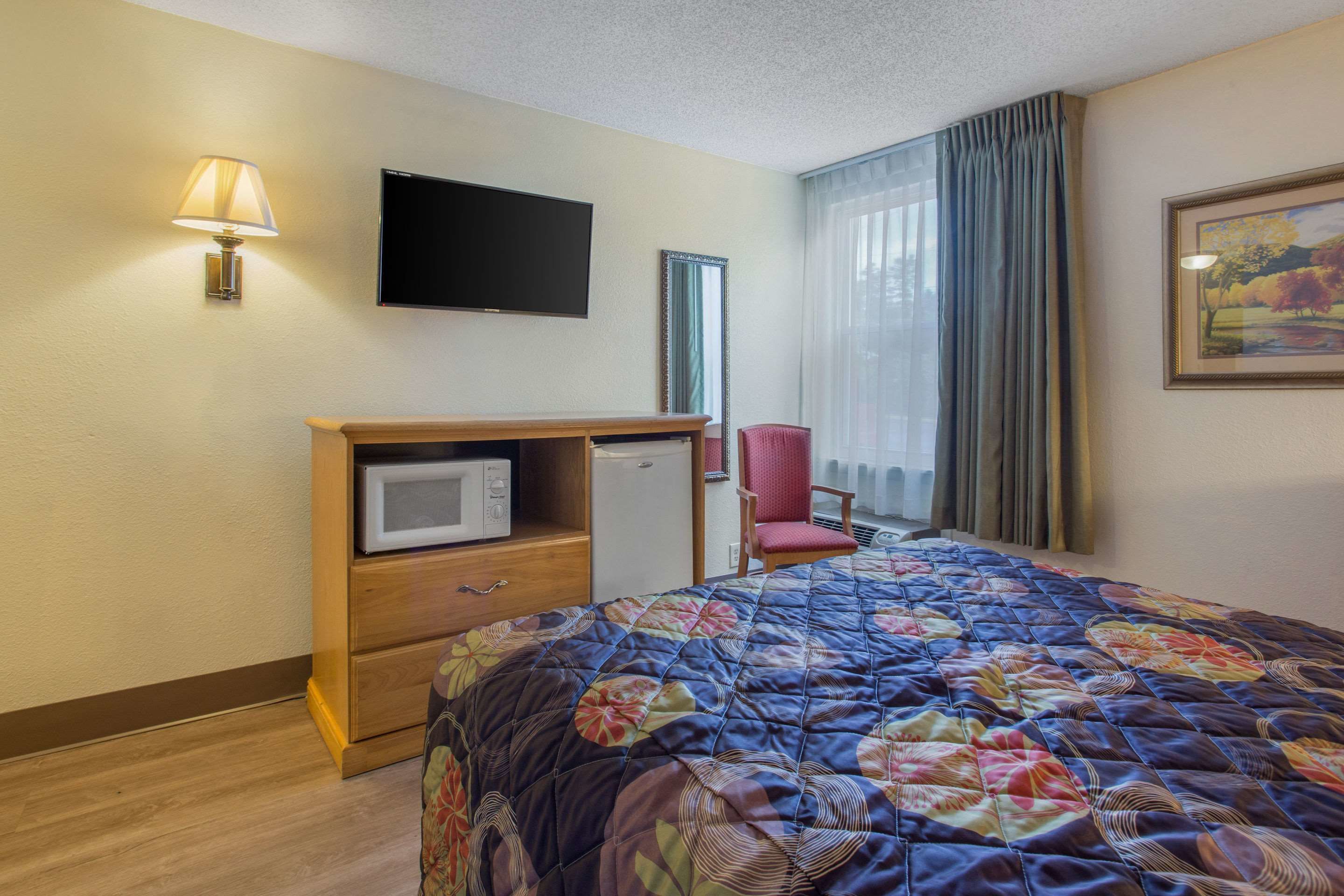 Quarto de hotel com cama, televisão, micro-ondas, cadeira e janela com cortinas.
