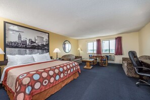 Habitación de hotel con cama, sofá, escritorio y silla. Se ve una ventana con cortinas y vistas a la silueta del horizonte de la ciudad.