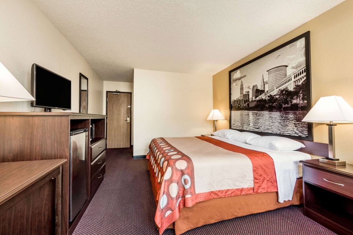 Ein Hotelzimmer mit Bett, Fernseher, Schreibtisch, Stuhl, Lampe und Tür.