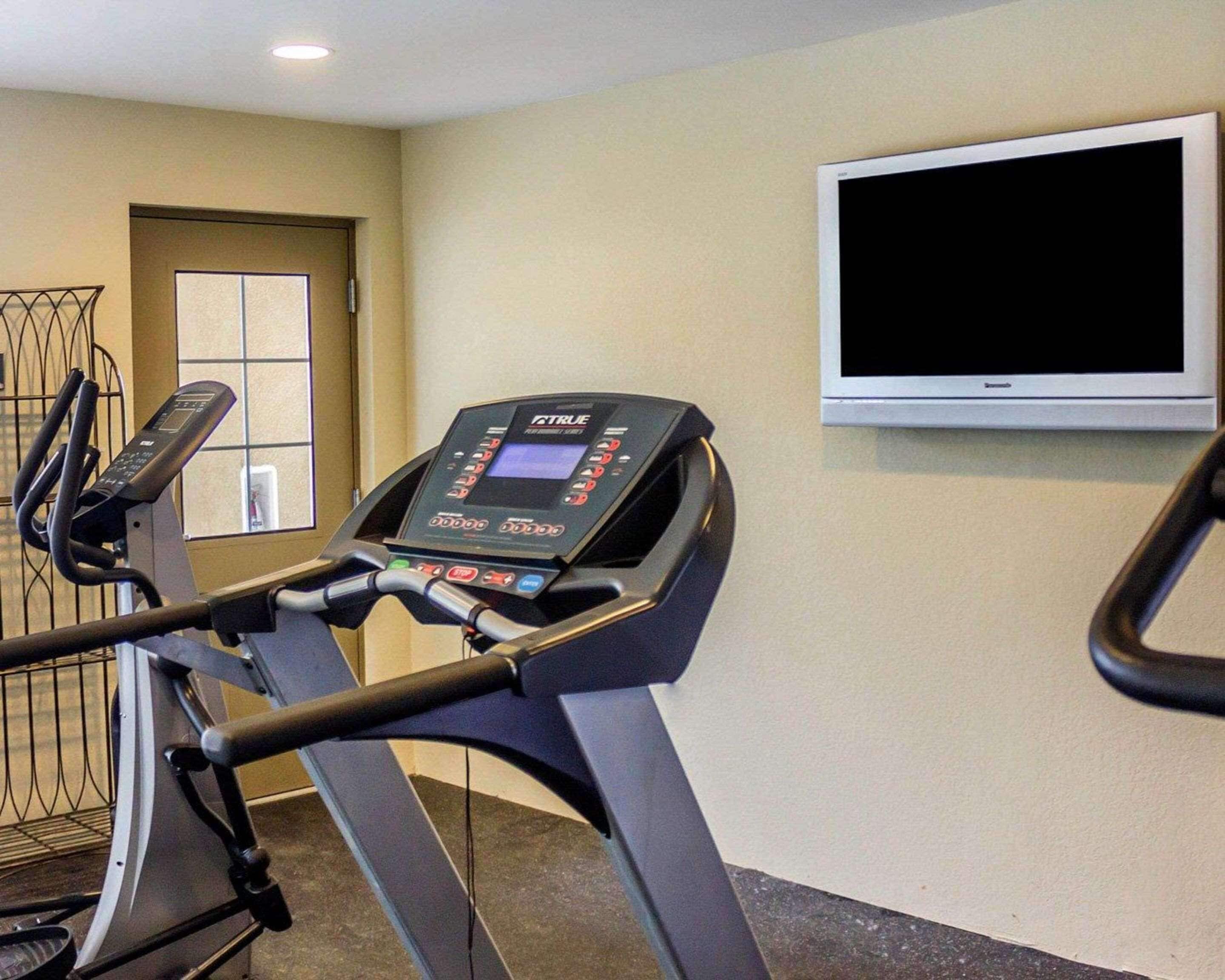Una cinta de correr con pantalla digital, una ventana y un televisor en la pared.