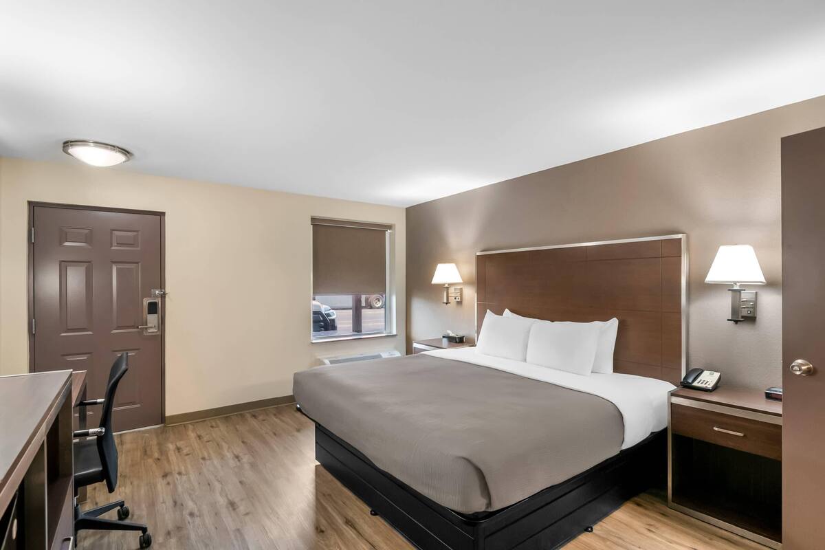 A hotel room with a bed, desk, chair, and two bedside lamps.