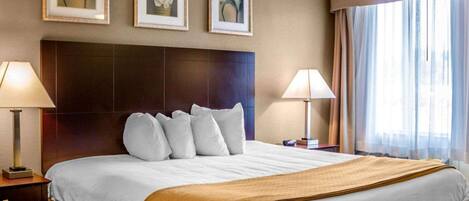 Una habitación de hotel con una cama grande, dos lámparas de noche, un cabecero y tres cuadros con motivos florales en la pared.