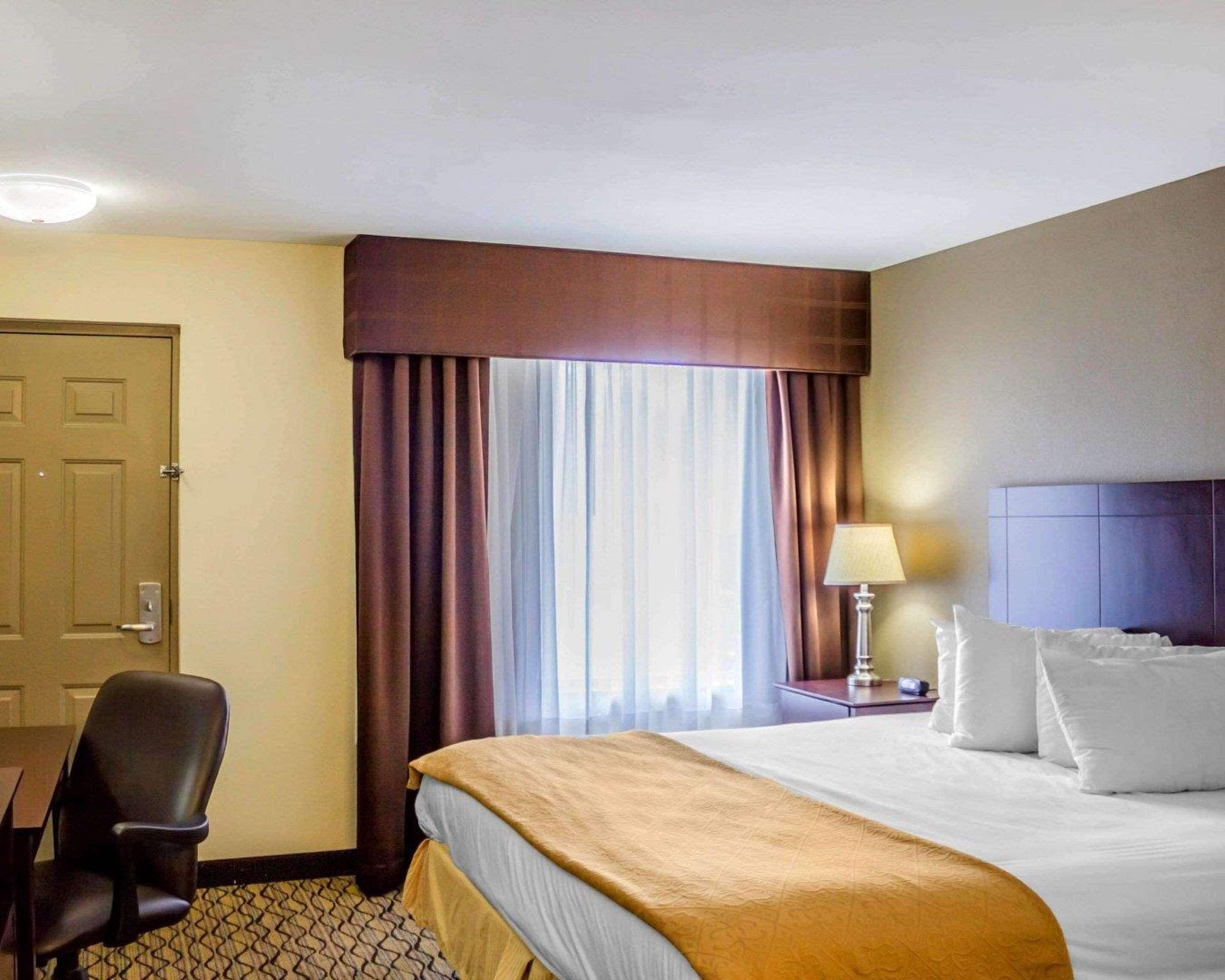 A hotel room with a bed, a desk, a chair, a lamp, and a window with curtains.